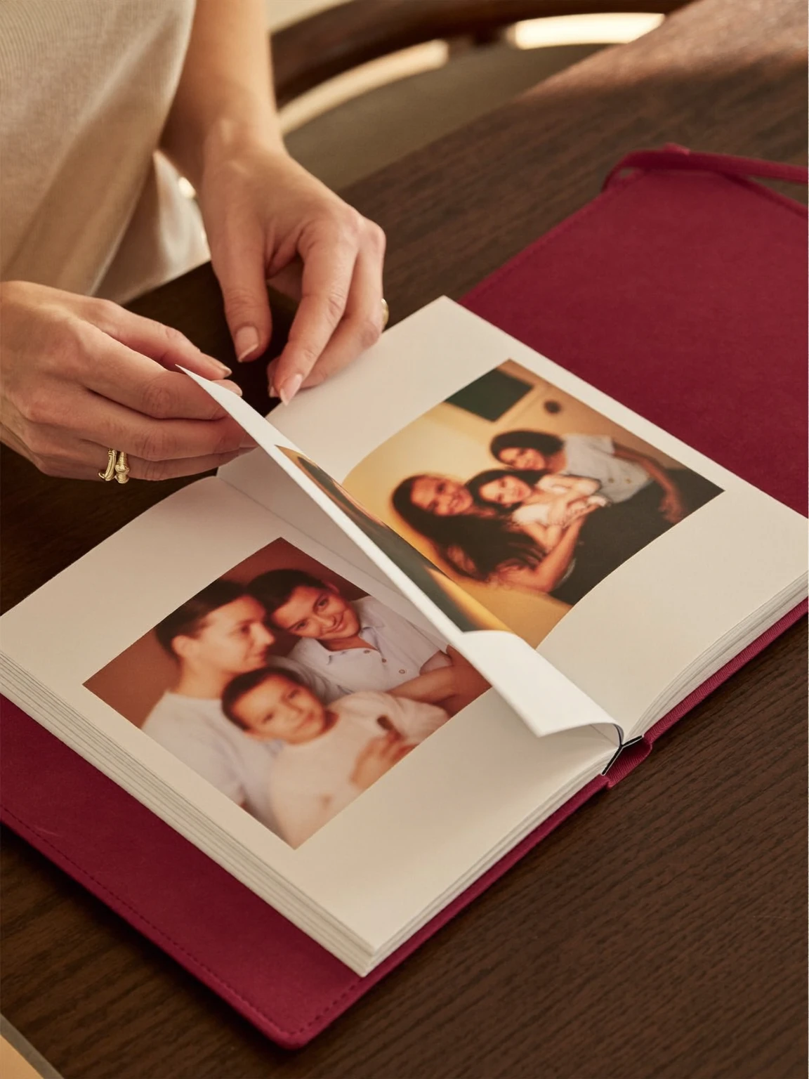 Mains qui tournent la page d’un album relié bourgogne ouvert sur des photos de famille.