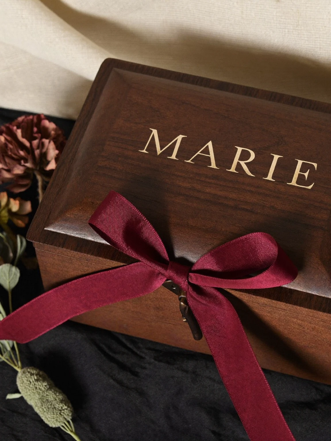 Couvercle d’un coffret en bois gravé « Marie » en lettres dorées, noué d’un ruban bourgogne.