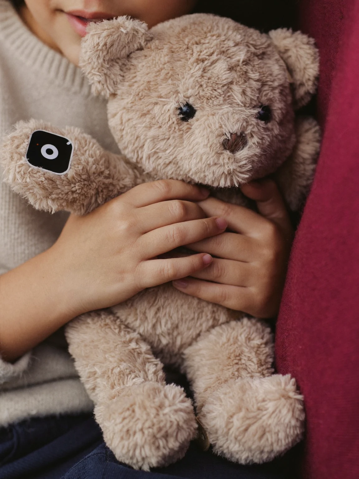 Enfant qui serre contre lui un ourson en peluche muni d’un bouton sonore sur la patte.