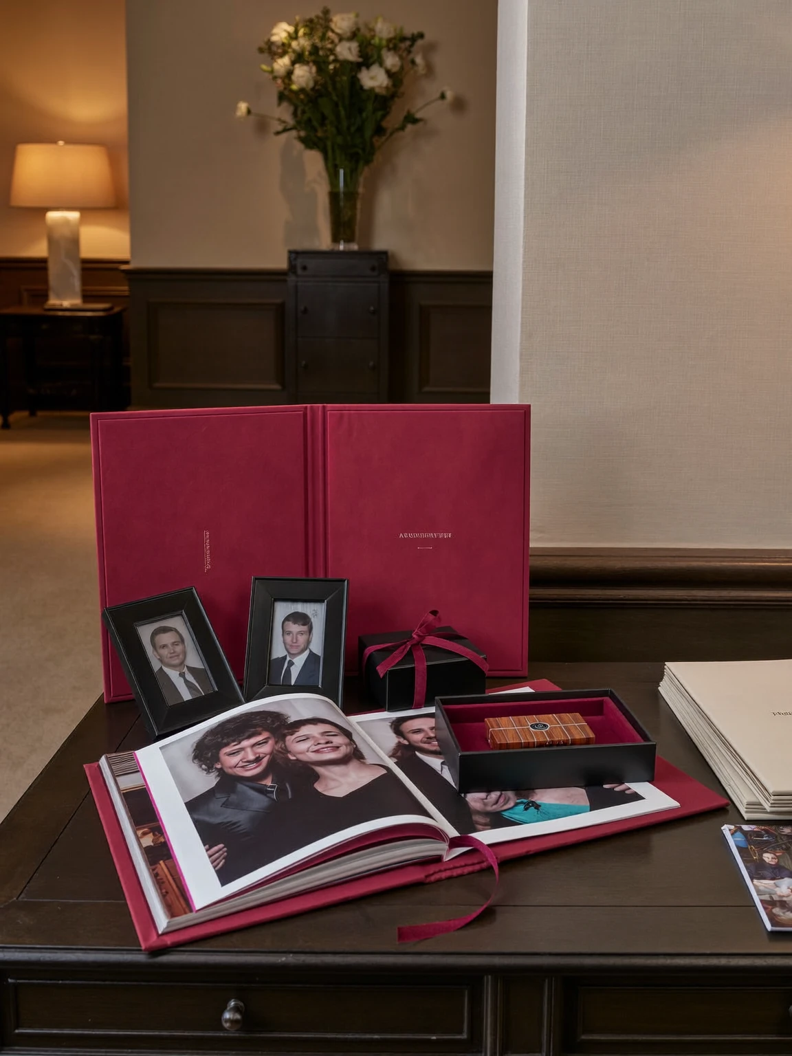 Kit souvenir présenté sur une table dans un salon élégant : album bourgogne ouvert, cadres photo, écrin avec clé USB et petite boîte nouée d’un ruban.